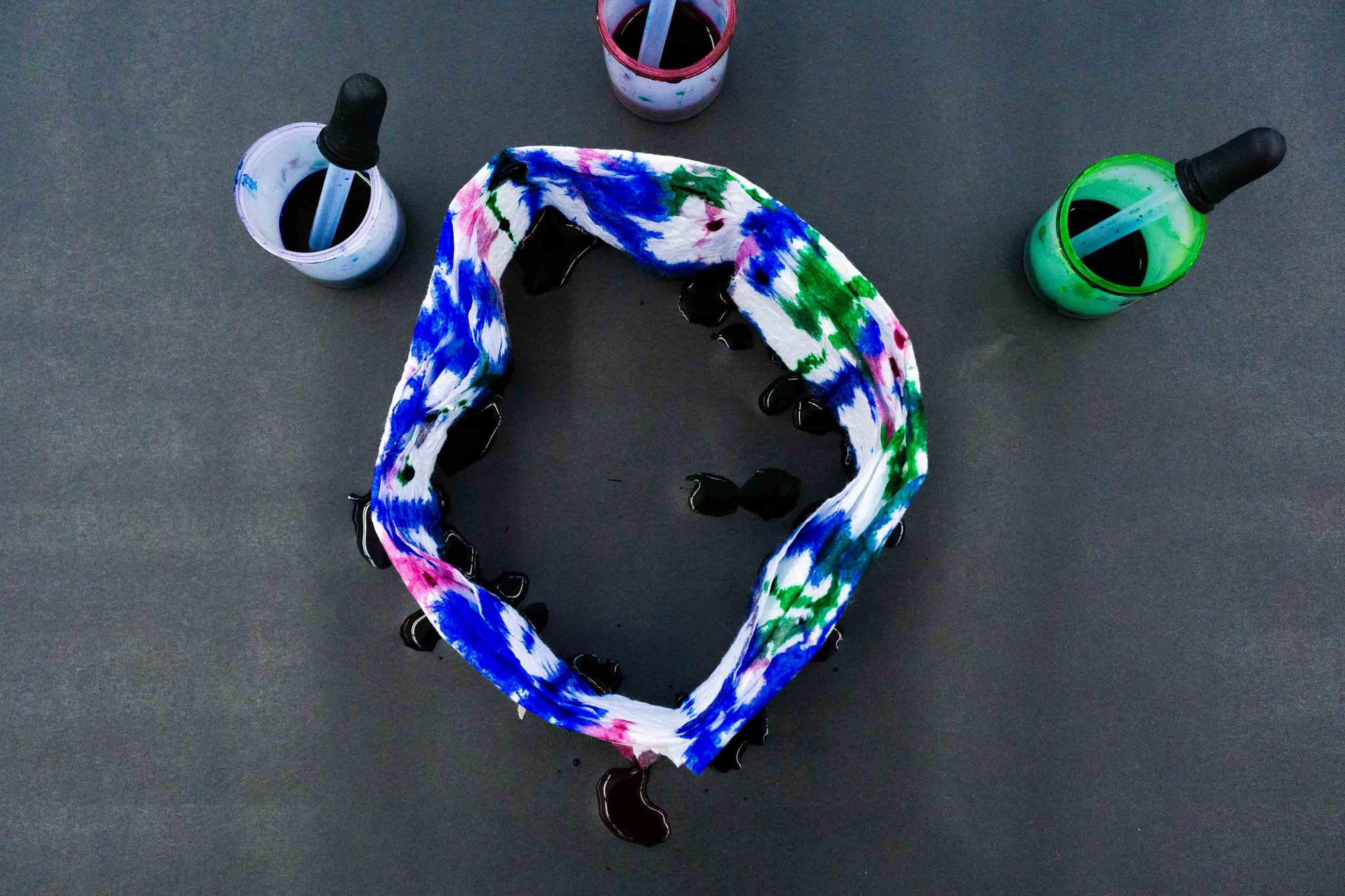 Photo of a colorful ring of paper with ink drips on it and containers with ink and droppers around it