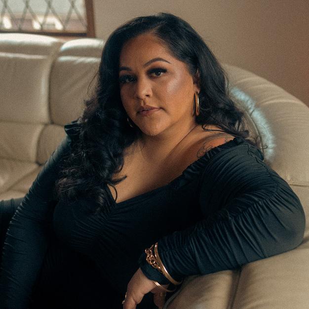 A woman in a dark dress leaning against the back of a couch and looking at the viewer